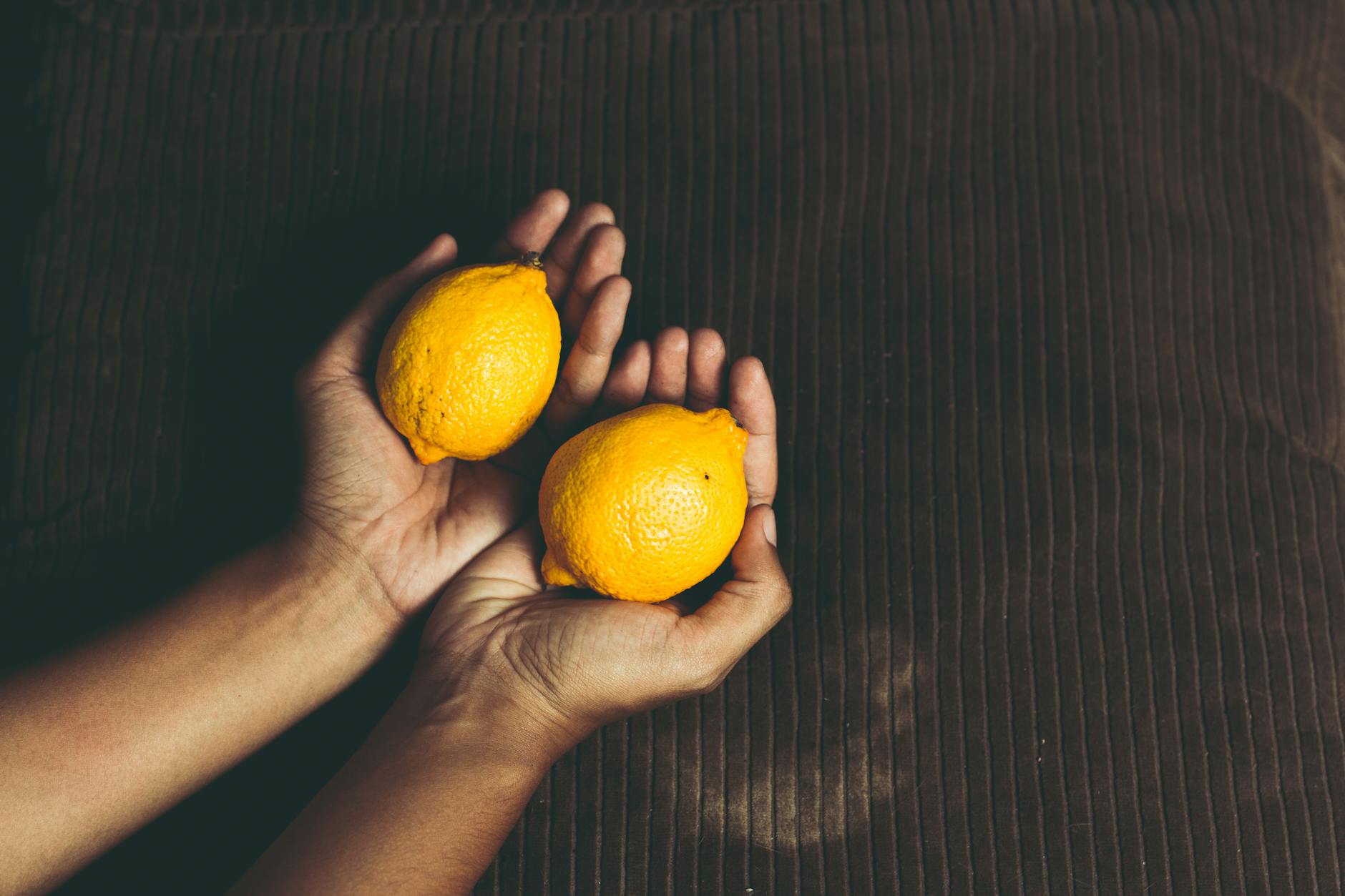 Fresh lemons held in cupped hands on a brown surface, symbolizing renewal and intimacy