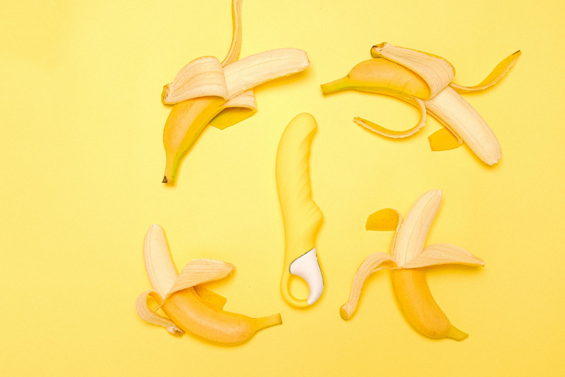 Yellow silicone lemon vibrator surrounded by fresh peeled lemons on a bright yellow background