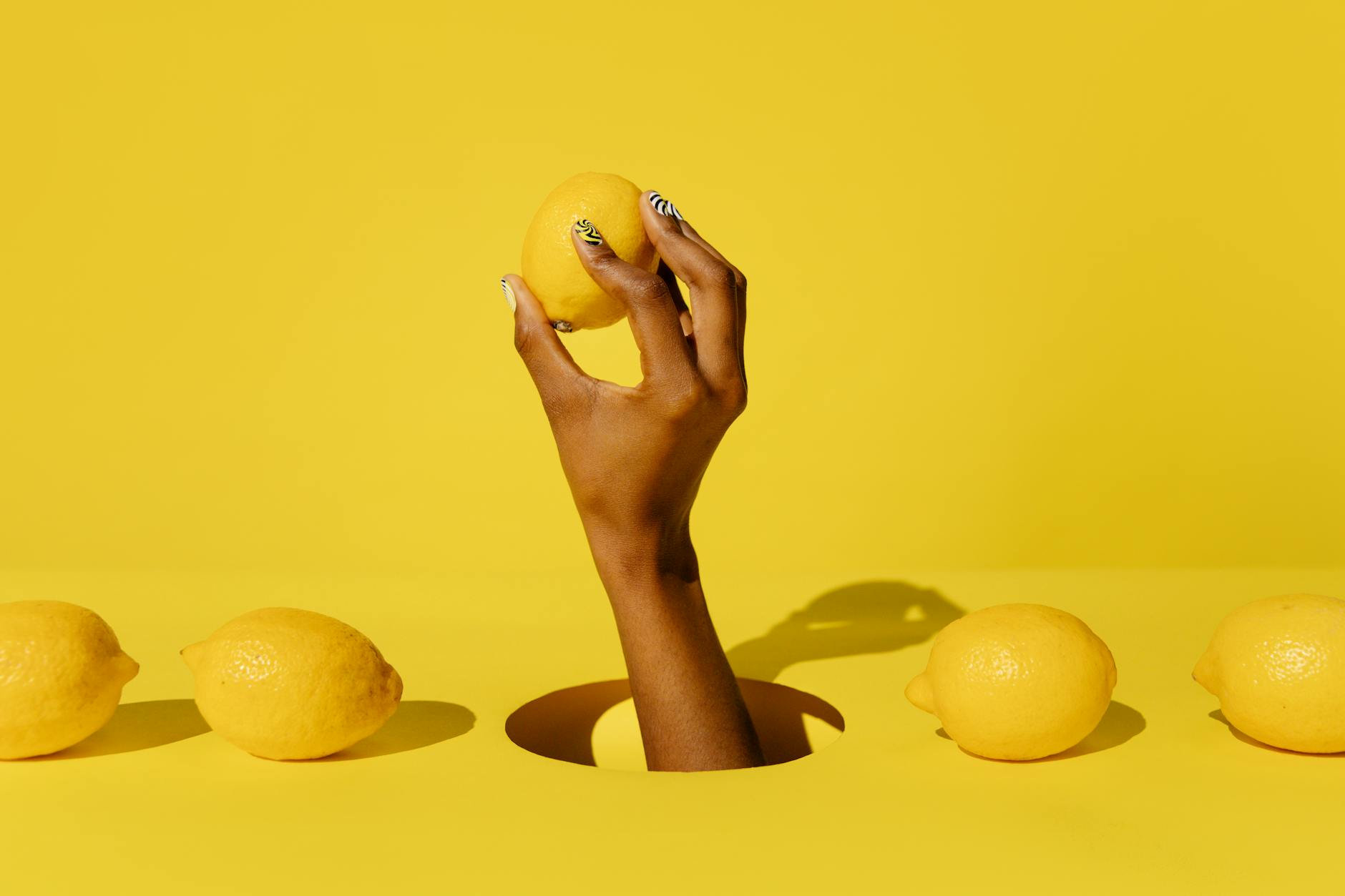 A fresh lemon held in hand against a bright yellow background, symbolizing accessible pleasure