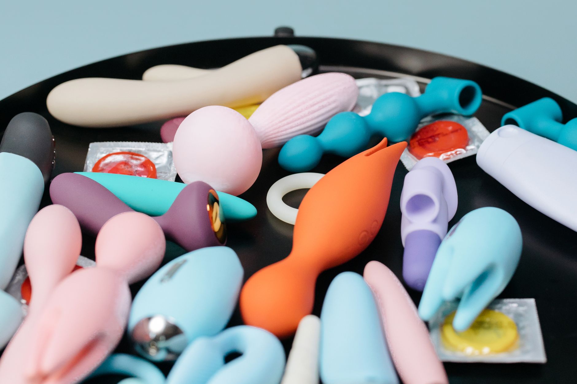 A vibrant collection of various silicone vibrators on a black tray, featuring diverse shapes and colors