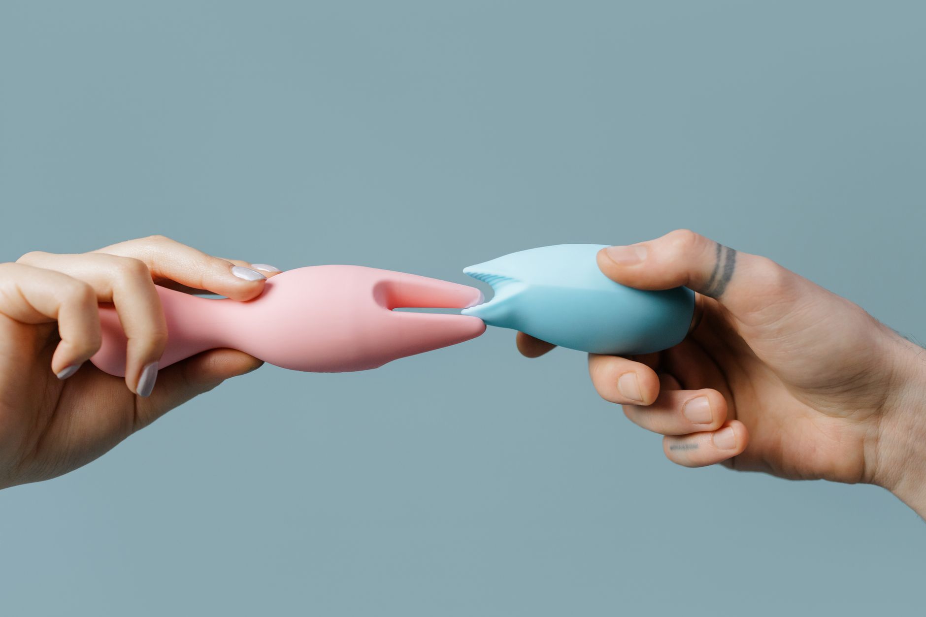 Hands holding silicone vibrators in pastel colors against a warm background