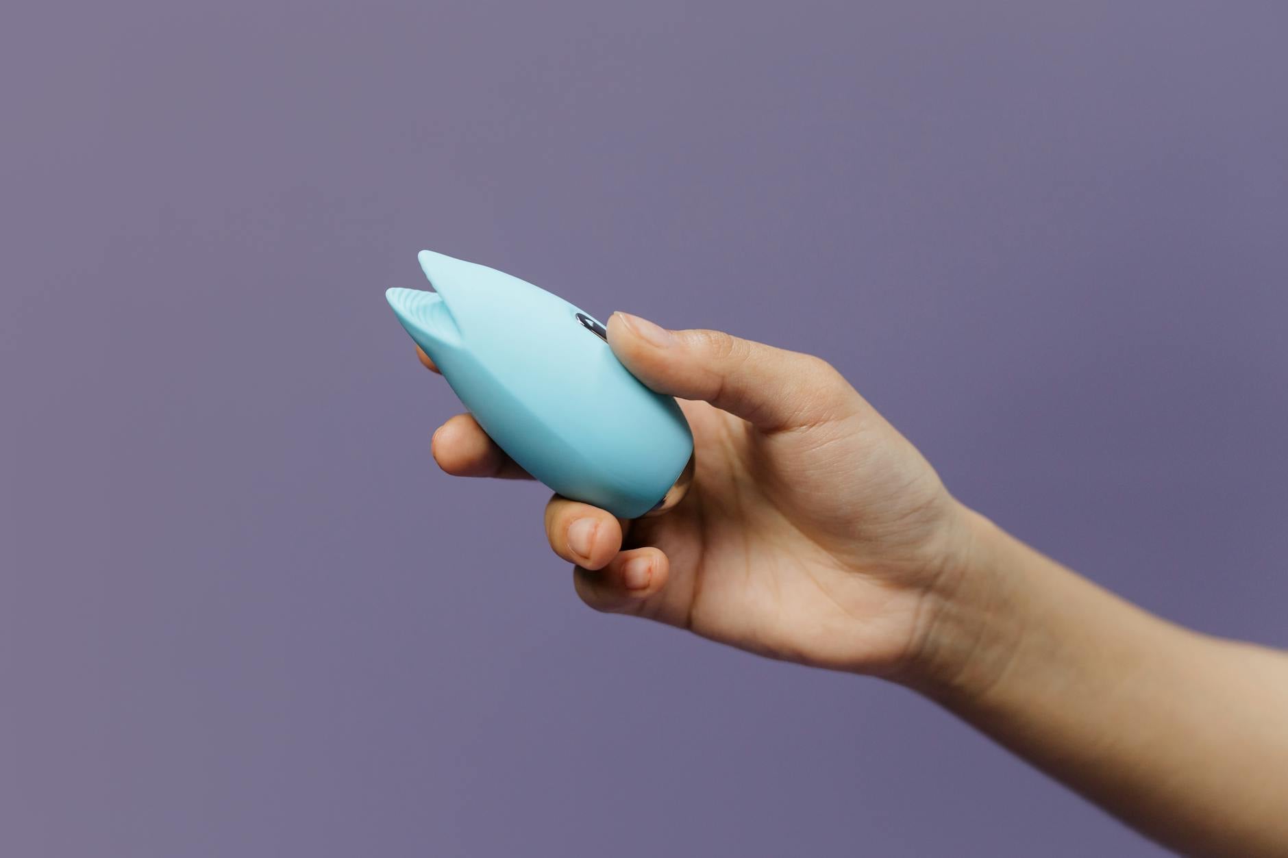 Hands holding a blue personal vibrator against a knitted sweater